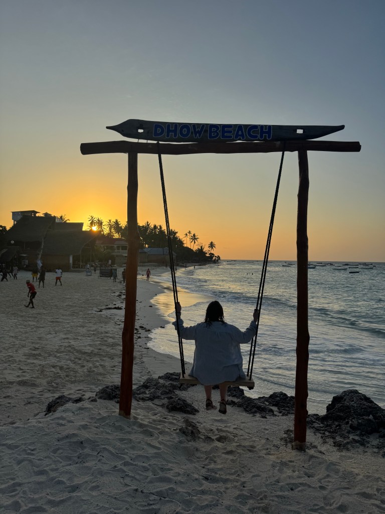 A woman (me) photographed from behind on a swing, on a tropical beach.