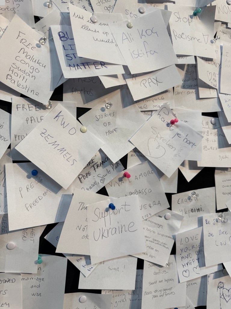 People's wishes written on square white pieces of paper, pinned to a board