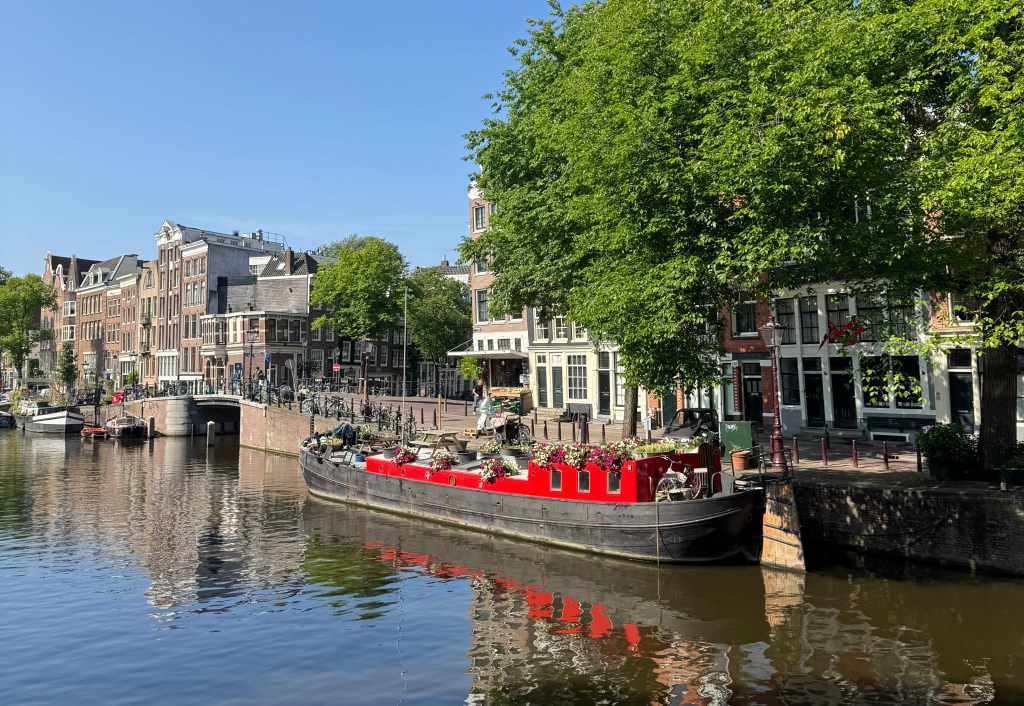 A red barge on the Prinsengracht canal in Amsterdam. It's a clear sunny day.