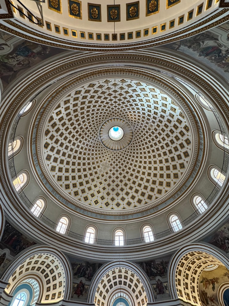 An ornate round roof of a church in Malta. It has a criss-cross white pattern and lots of small windows around the edge.