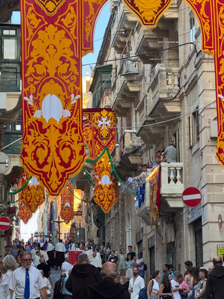 A busy street in Valetta, Malta with large orange and red banners strung up across the street