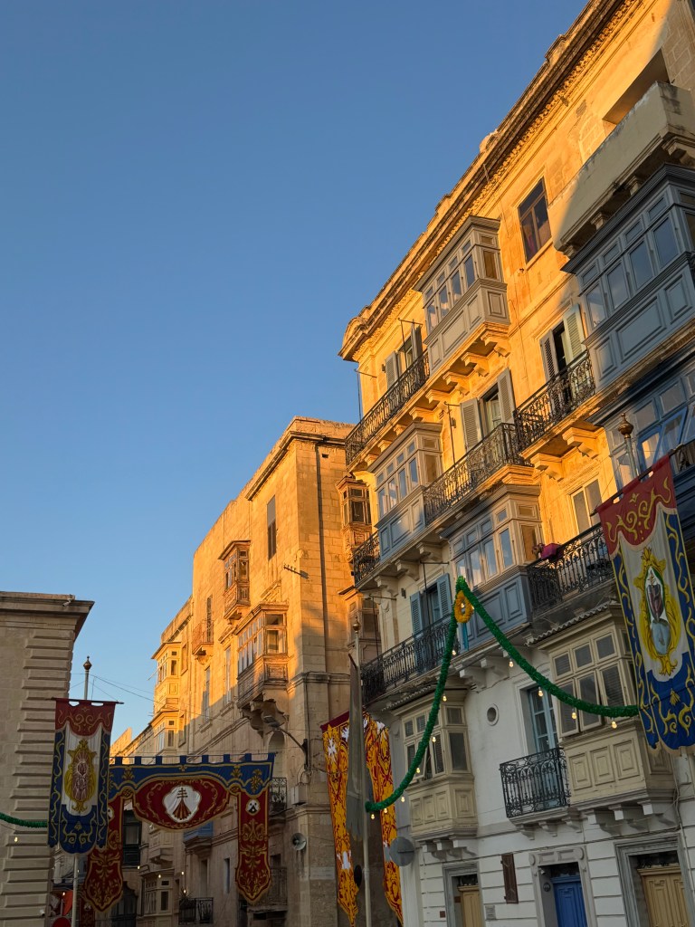 The dusk sun hits historic buildings in Valetta, Malta, producing a warm orange glow across the balconies