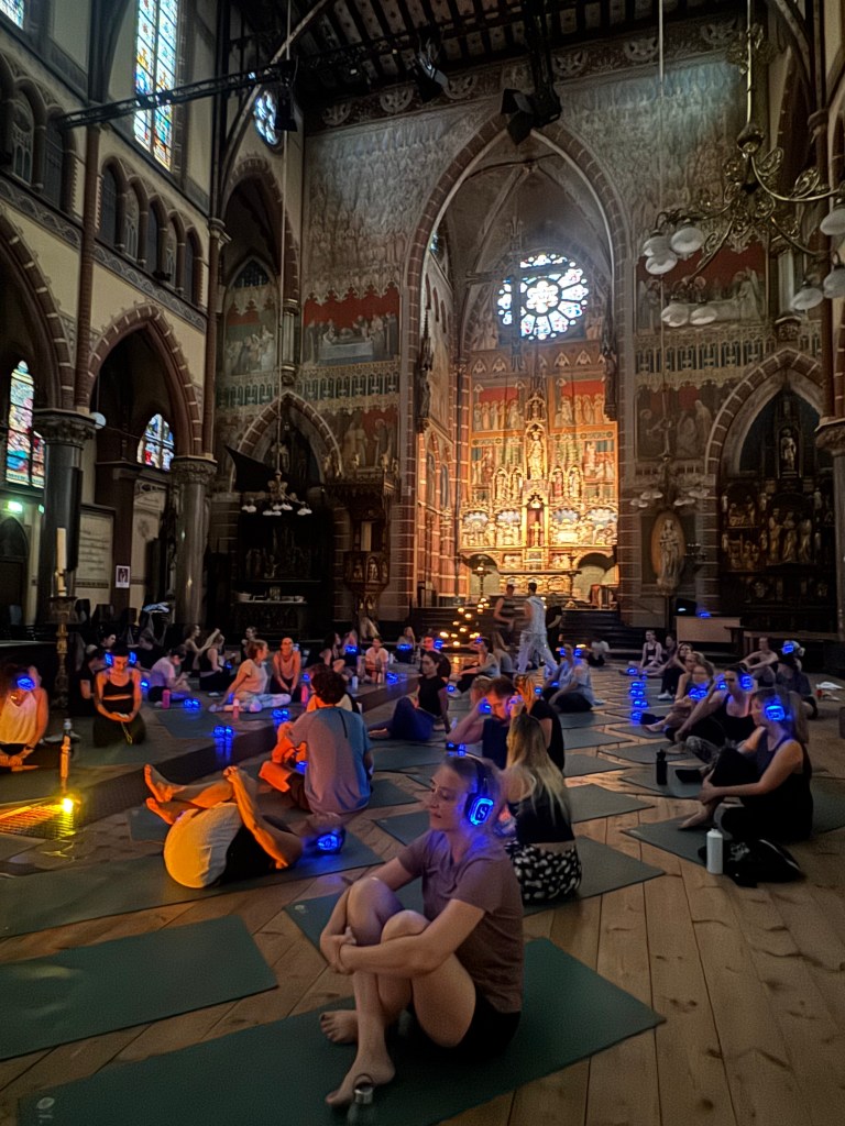 People sit on yoga mats on the floor of an atmospheric old church, wearing silent disco headphones