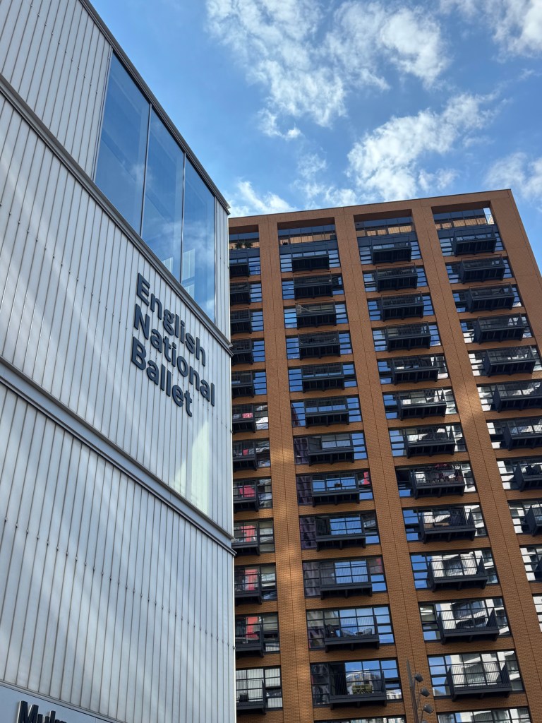 Exterior view of the English National Ballet building alongside a modern apartment complex, with a blue sky and clouds in the background.