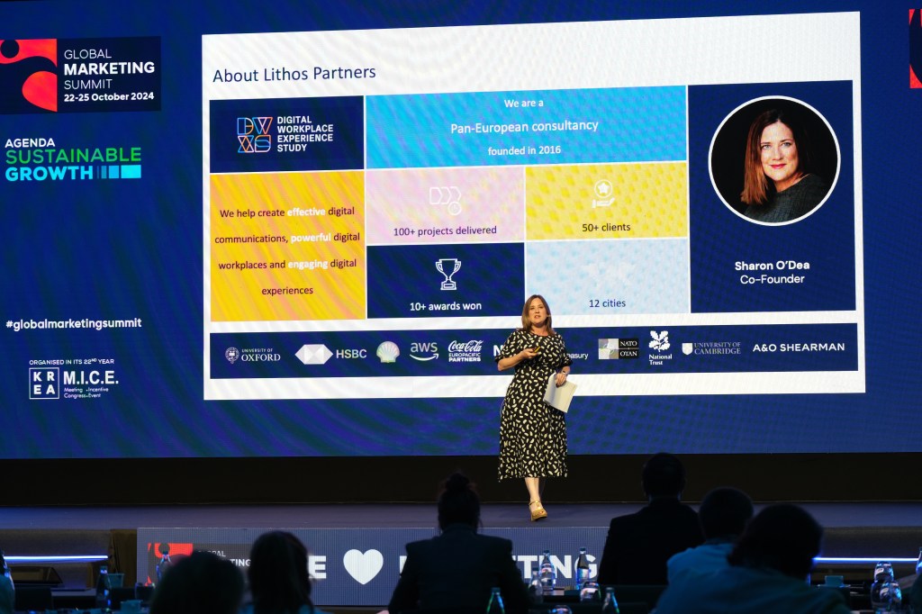 Sharon O'Dea on stage in a black and white dress with a large powerpoint slide behind