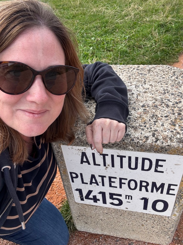 A person with sunglasses posing next to a stone sign indicating an altitude of 1415 meters.