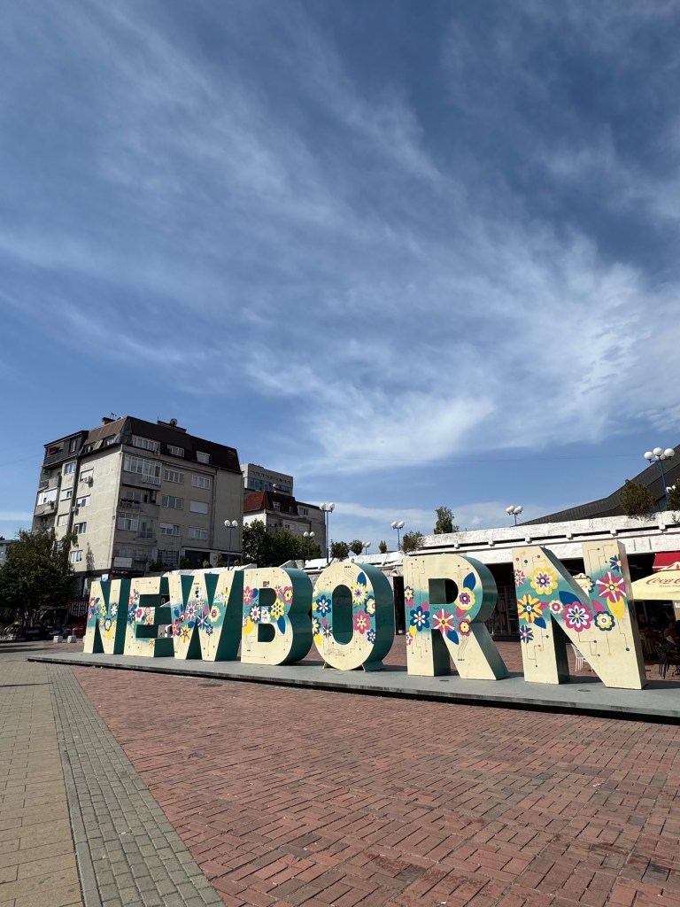 Colorful large letters spelling 'NEWBORN' in a public square in Pristina, Kosovo, with a blue sky and buildings in the background.