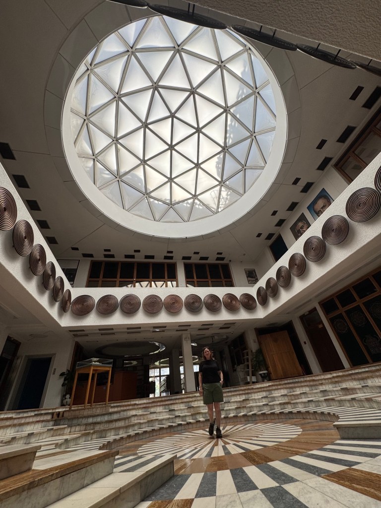 Interior view of a modern building featuring a geometric skylight and circular patterned flooring, with a person standing in the center.