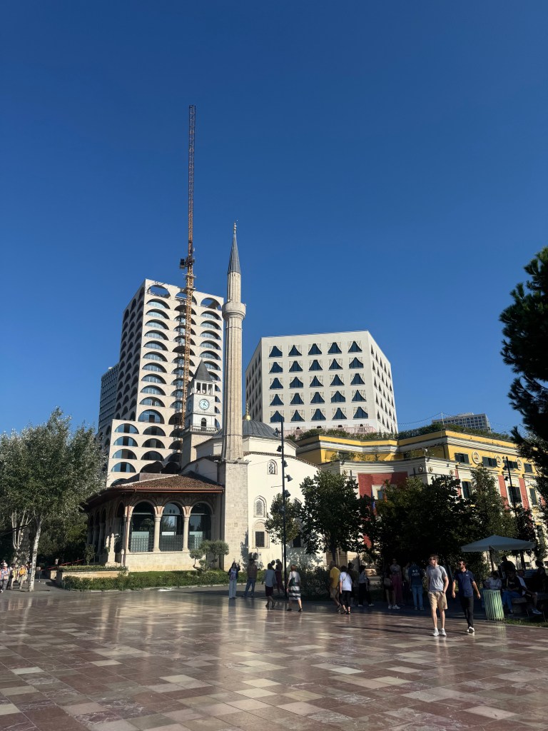 A blend of modern and traditional architecture, featuring a mosque with a tall minaret alongside contemporary buildings under a clear blue sky.