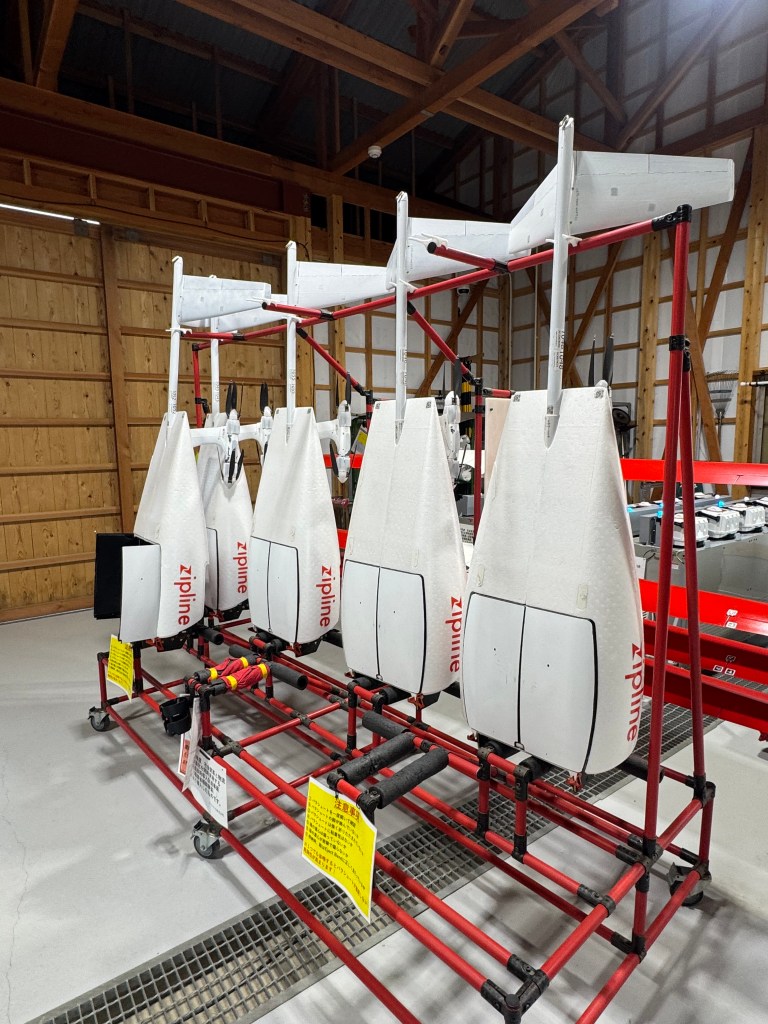 A display of drones used for medical delivery, arranged on a red metal rack in a spacious indoor facility.