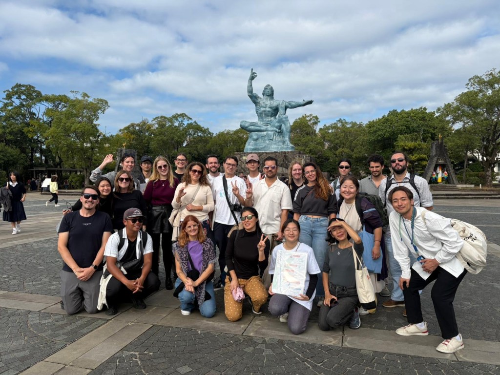 Group photo in Nagasaki, Japan, with a statue in the background and participants posing together in a relaxed outdoor setting.