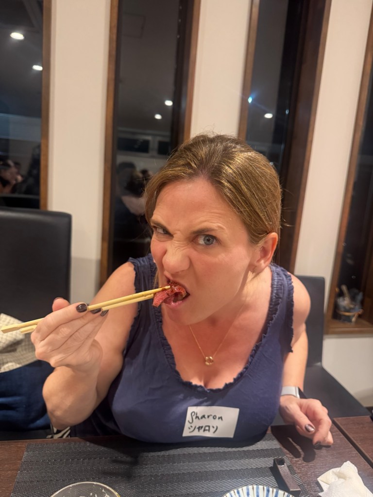 A person making a funny facial expression while holding food with chopsticks, sitting at a dining table with a name tag visible.