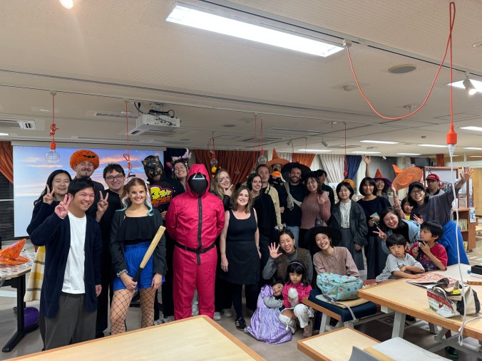 Group photo of adults and children dressed in various Halloween costumes, posing together in a festive environment.