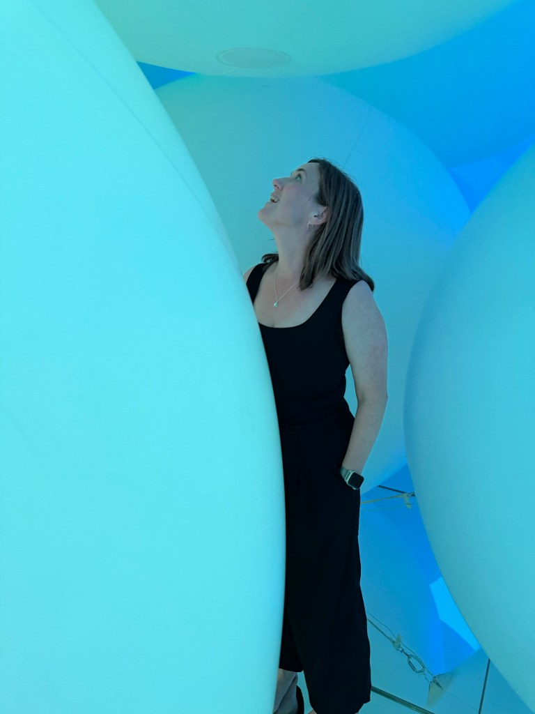 A person standing amidst large blue spherical structures, looking up with a smile.