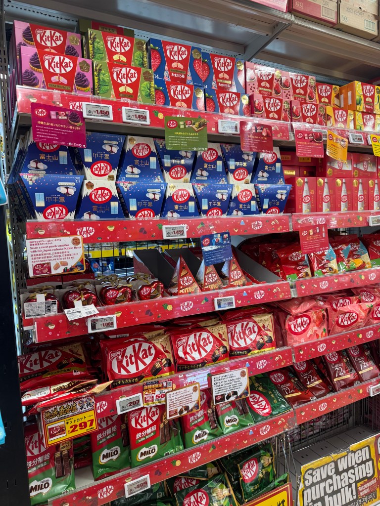 A display of various flavored KitKat chocolates stacked on shelves in a store in Japan.