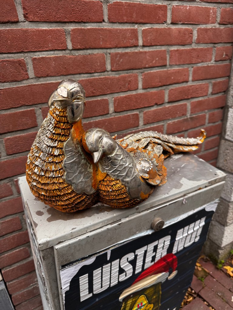 A decorative sculpture of two stylized birds sitting on a metallic box against a brick wall.