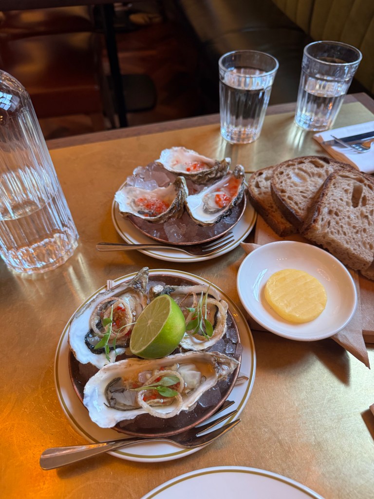 A stylish platter of fresh oysters served with lime and garnishes, accompanied by a side of butter and slices of bread on a table.