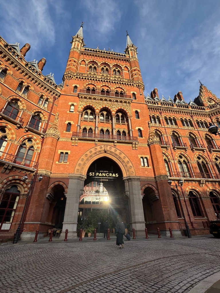 The exterior of St. Pancras Railway Station in London, showcasing its ornate brick architecture and tall spires under a clear blue sky.