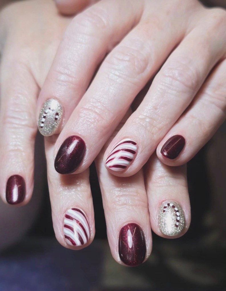 Close-up of manicured hands with festive nail designs featuring deep red, gold glitter, and candy cane stripes.