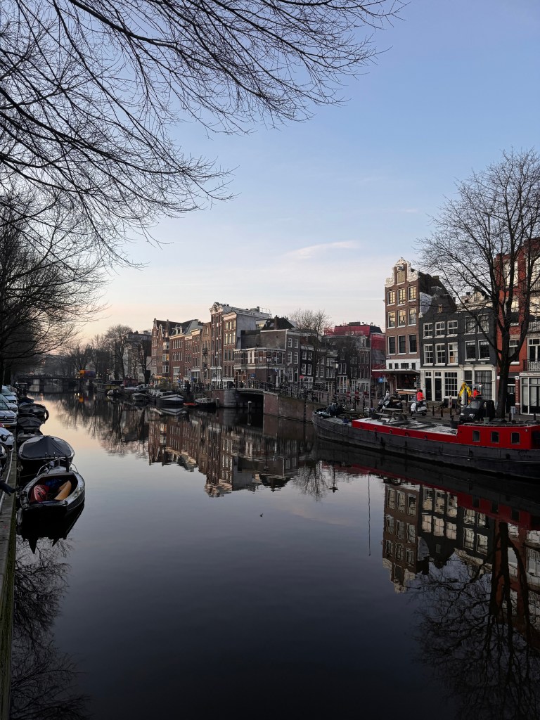 Scenic view of a canal in Amsterdam, featuring historic buildings reflected in the water during early evening.
