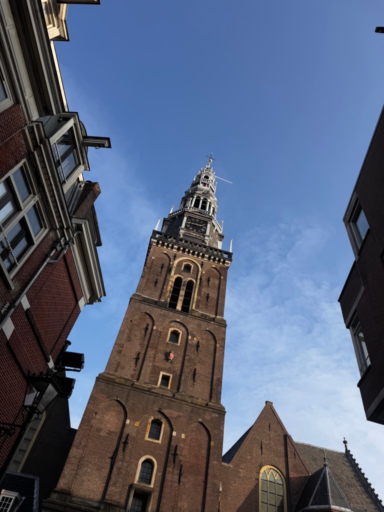 View of a tall brick tower against a clear blue sky, surrounded by historic buildings.