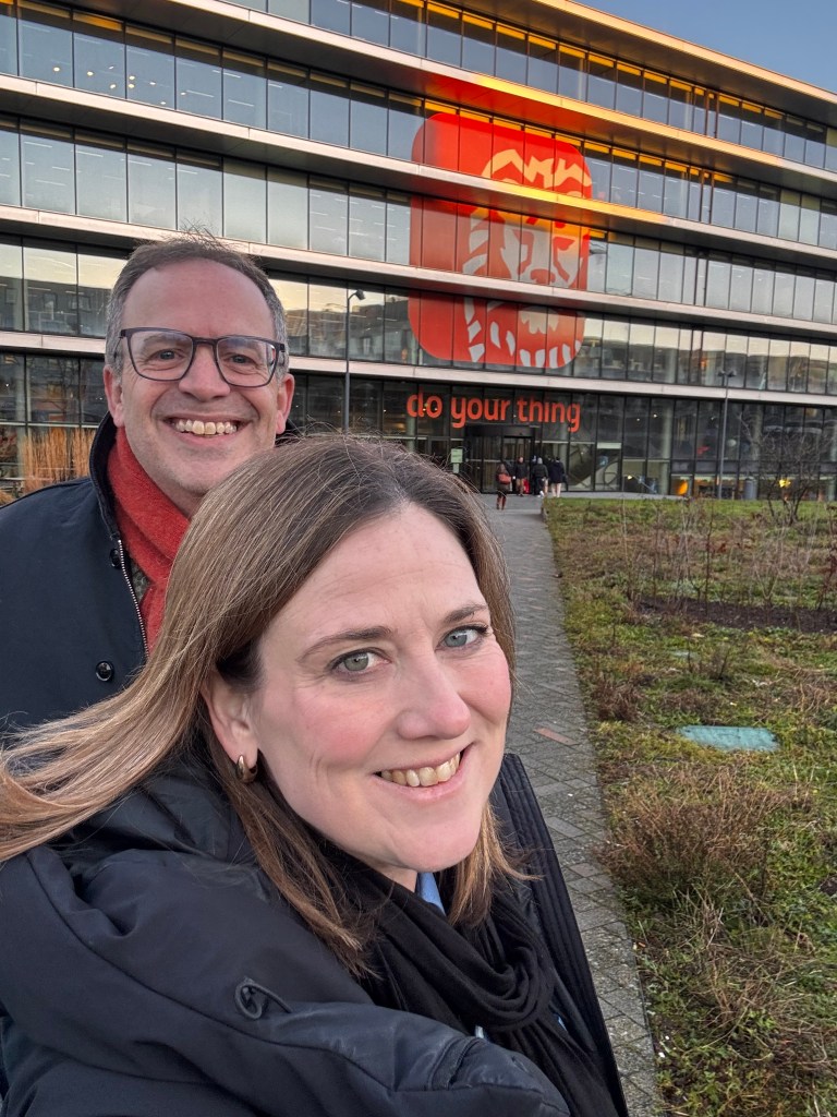 Two people posing for a selfie in front of a modern building with large windows and the words 'do your thing' displayed prominently.