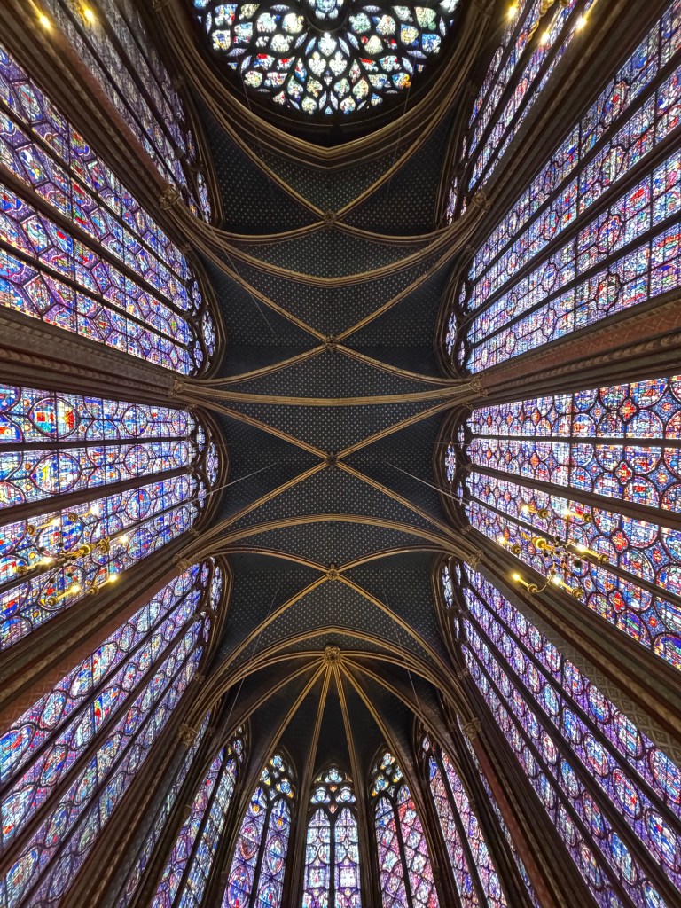 A view of the stunning stained glass windows and vaulted ceiling inside Sainte-Chapelle in Paris, showcasing intricate designs and vibrant colors.