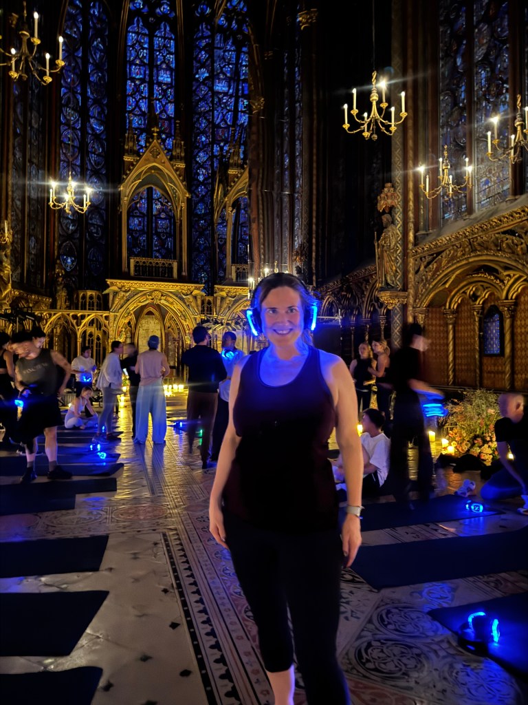 A group workout session inside a historic chapel, with participants wearing glowing headphones. The ornate interior features intricate stained glass windows and soft lighting, creating a serene environment.