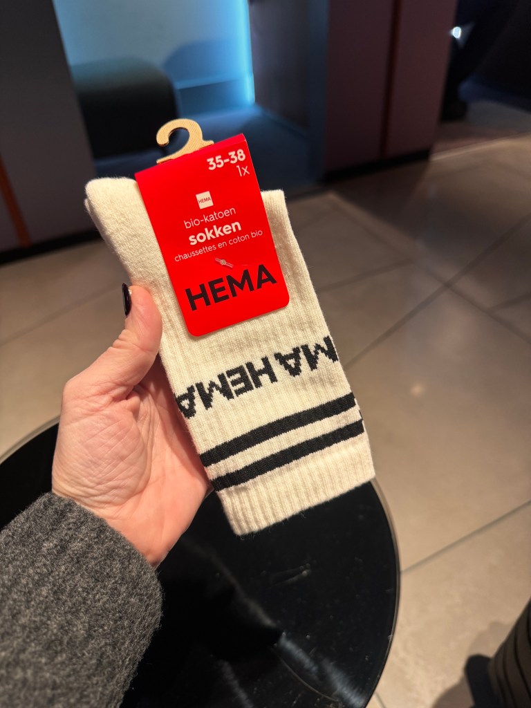 A person holding a pair of cream-colored socks with a tag indicating size 35-38 and made from organic cotton, featuring the brand name 'HEMA' and black stripes.