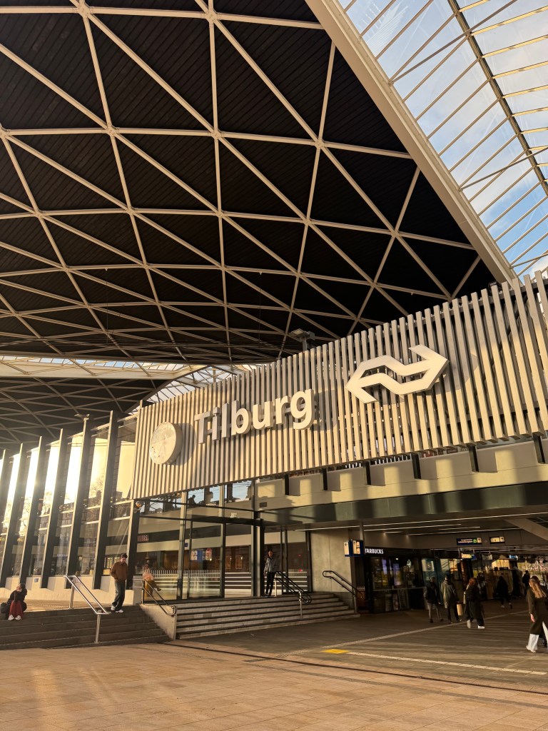Exterior view of Tilburg train station featuring a modern architectural design with a prominent sign displaying 'Tilburg'.